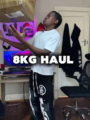 A young man stands in a room and throws a large cardboard box upwards, looking up with a focused expression. The text overlay '8KG HAUL' is prominently displayed. The room appears to be a bedroom, with a computer setup and items like a hoodie and a sign visible in the background.