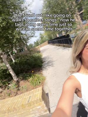 A selfie shot, with a woman on the right side looking towards the camera with a walkway and green trees in the background.