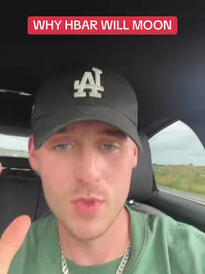 A man in a black LA Dodgers cap, green shirt, and silver necklace sits inside a car, looking towards the camera. Text overlay on the top reads 'WHY HBAR WILL MOON'. The background appears to be a grassy area.