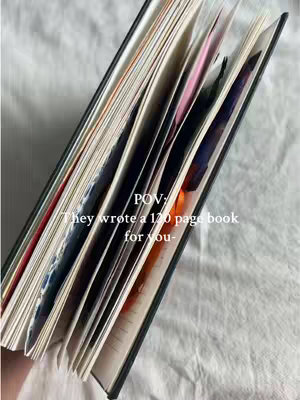 An open journal is angled diagonally across a white surface. The journal's pages are visible, with a variety of colored pages or inserts. Text is overlaid near the top left of the image.