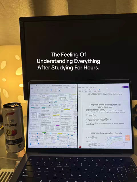 A laptop displaying a study document with a can of Celsius energy drink to the left. The laptop is open, showing multiple pages of text and diagrams, likely academic notes and formulas. The background includes a monitor, a table, and soft lighting. The overall composition suggests a study environment, the monitor, and the laptop both being front and center.