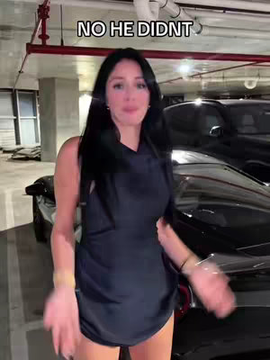 A woman is standing in a dimly lit parking garage, with a sleek black car behind her. She's wearing a dark, sleeveless dress and looking towards the camera with a slight smile. Text overlayed at the top reads "NO HE DIDNT".