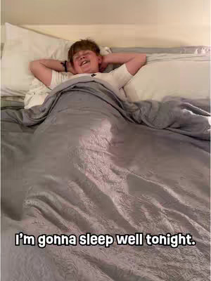 A young boy lies in bed, smiling with his hands behind his head, under a grey blanket. The text overlay reads, 'I'm gonna sleep well tonight.'
