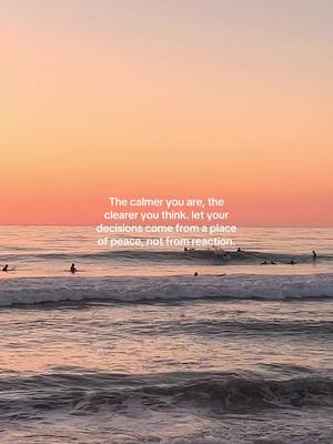 The image captures a serene ocean scene during sunset. The sky transitions from a soft peach to orange hues, reflecting onto the water. Gentle waves lap the shore, with several distant figures, likely surfers, dotting the water. A text overlay in the center of the image offers a quote regarding peace and decision-making.