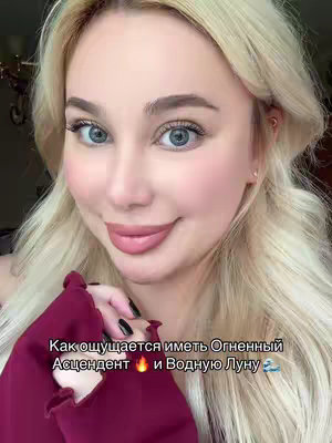 A close-up shot features a fair-skinned woman with blonde hair and blue eyes. She is holding a dark red garment, with text overlaid at the bottom of the image. The background is slightly blurred.