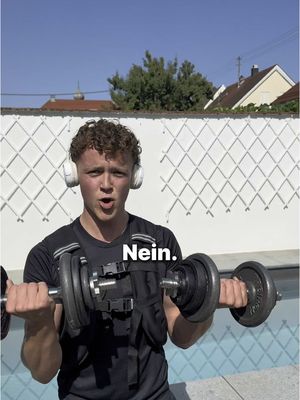 A young man with curly hair is holding two dumbbells, with a surprised expression. He wears a black top, and headphones and the background shows a swimming pool and a house behind a wall.