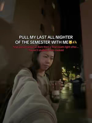 A selfie video shows a young woman in an outdoor setting at night. She holds a clear cup with a dark beverage. Text overlays appear at the top, including the title and additional details about studying. The image is slightly blurred, indicating a handheld shot.