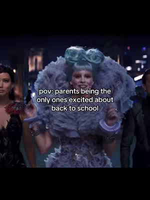A scene from a movie, featuring a woman with extravagant hair and clothing, likely an antagonist. The text overlay reads 'pov: parents being the only ones excited about back to school'. The woman in the center wears a large, feathery, and ornate outfit with a blue wig. The background is blurred, suggesting a large building or event setting with lights and colors. Other characters are partially visible.