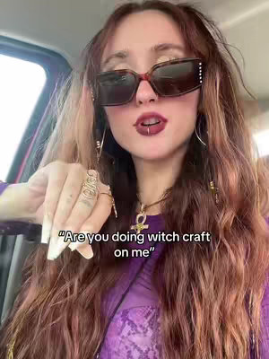 A woman with long, wavy auburn hair, wearing large sunglasses and a purple top. A text overlay asks, "Are you doing witch craft on me?"