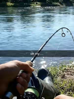 A first-person view of someone fishing, holding up the rod and reel with the water and the shoreline in the background.