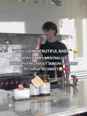 A young man, likely in his late teens or early twenties with short, dark hair, is captured in a kitchen setting. He's holding a white cup to his mouth, appearing to take a drink. The background includes kitchen surfaces, cabinets, and a glimpse of sunlight. Text overlays reveal a romantic compliment.