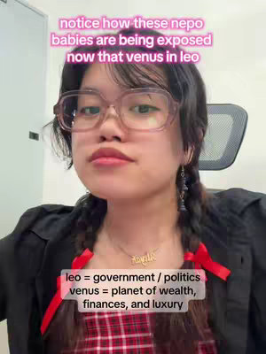 A young woman with glasses and two braids, wearing a black top and a red plaid shirt, looks directly at the camera. Text overlays explain that the video is about nepo babies being exposed during the transit of Venus in Leo, and that Leo represents government/politics while Venus represents wealth, finances, and luxury. A necklace with the name "Kayli" is seen.