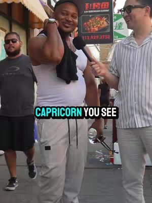 An outdoor scene with three men: one in a white tank top and grey pants is holding a microphone and being interviewed, another man is standing on the left wearing a black t-shirt and wearing sunglasses, and a third man on the right in glasses is also facing the interviewee. Text overlayed on the image that says "CAPRICORN YOU SEE".