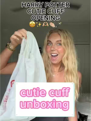 A woman with long blonde hair is holding up a clear bag with text overlaid on a white rectangular background, smiling widely while looking at the camera. Above her is the title "HARRY POTTER CUTIE CUFF OPENING" with various emojis. The background suggests a home setting.