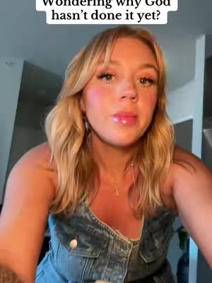 A woman with blonde hair and a denim top is seen in a close-up shot. The text overlay reads, 'Wondering why God hasn't done it yet?' The background is minimalistic with a door visible on the right side.