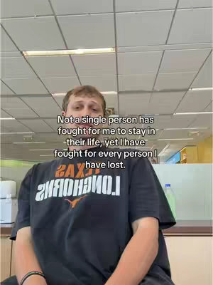 The cover image presents a front-facing shot of a young man wearing a black t-shirt with white text, likely a logo. The man is set against a plain office-like background, which includes rectangular ceiling panels and a desk. Text overlay is positioned over him, containing a reflective quote.