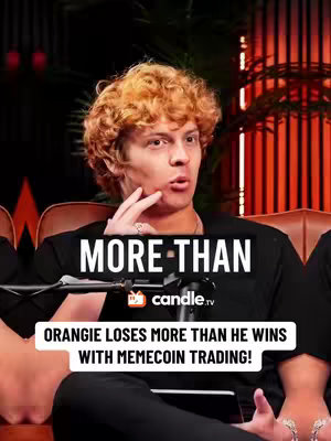 The cover image features a young man with curly, reddish-blonde hair. He is seated and facing forward, with his right hand raised to his chin and lips, suggesting contemplation or surprise. Overlaid on the image is a white banner with the text "MORE THAN". Below this, a black banner reads, "ORANGIE LOSES MORE THAN HE WINS WITH MEMECOIN TRADING!". The background appears to be a dimly lit room or studio, with what looks like plants and a red light source, adding depth and contrast.