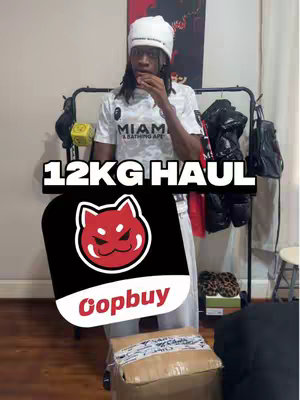 A young man stands in a room, holding a finger to his lips in a gesture, with clothing racks in the background. Overlayed on the image are the words '12KG HAUL' in bold white text, and a logo depicting a red, angry cat with a black background.