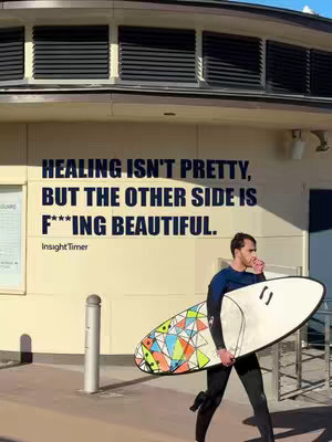A man walks along a sidewalk holding a surfboard. Behind him is a building with the text overlayed.