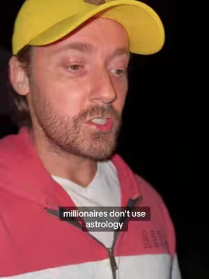 A man wearing a yellow cap and a red hoodie is speaking directly towards the camera. A text overlay at the bottom states, "millionaires don't use astrology."
