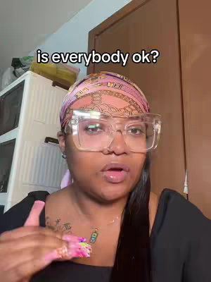 The cover image shows the a woman with dark skin looking at the camera. She is wearing a black top, large clear-frame glasses, and a pink and patterned headscarf, plus jewelry. The text overlay reads 'is everybody ok?' in a white font.