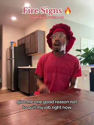 A person is holding the camera, with a kitchen in the background. The person is wearing a red headscarf and shirt, and has round glasses. Text overlays read "Fire Signs" at the top and a question below.