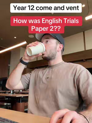 A man drinks from a white paper cup, the camera focuses on him. He wears a baseball cap and a t-shirt. Text overlays on the top of the image, with a red bar also adding more text.