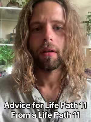 A man with long, wavy brown hair and a beard looks directly at the camera. The image is taken from the chest up, and the background includes shelves and plants in a room. Text overlayed on the image reads, "Advice for Life Path 11 From a Life Path 11".