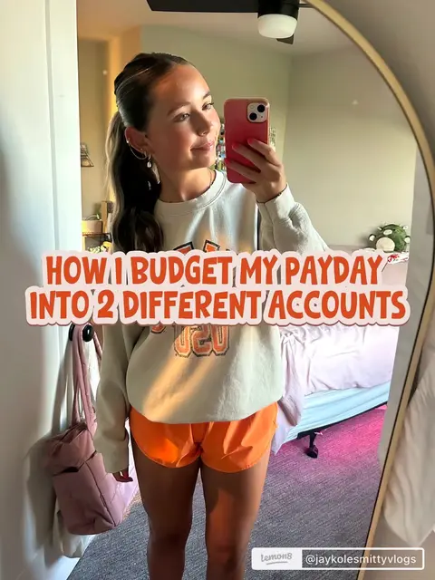A woman is taking a mirror selfie. She is wearing a light sweatshirt an orange skirt. The mirror she is using has a golden frame. The background has a bed and a sign.