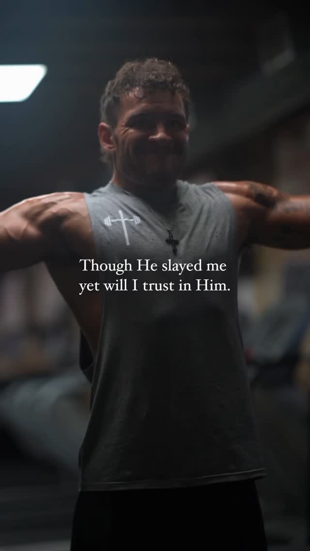 The cover image is a medium shot of a muscular man in a gym setting. He is wearing a gray tank top with a cross and weightlifting symbol. The man has his arms extended out to the sides. The background is slightly blurred, revealing gym equipment and dark tones. A text overlay reads, "Though He slayed me yet will I trust in Him."