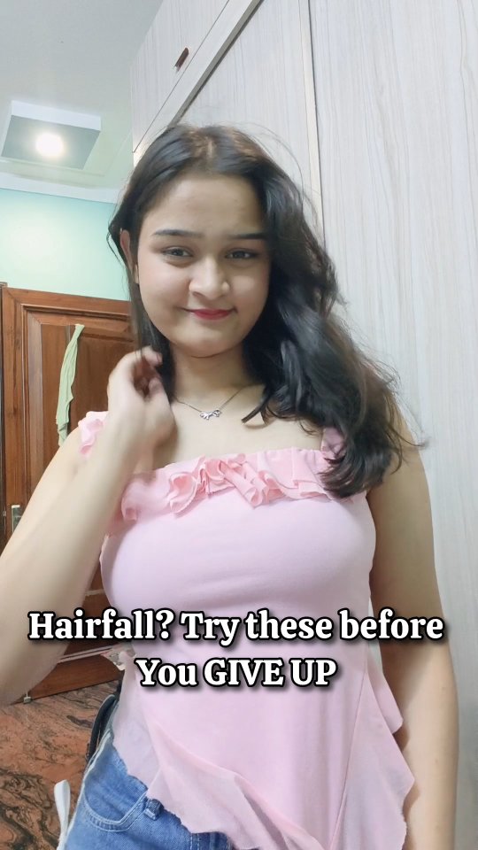 A woman in a pink top poses for the camera with her hair styled down. The text overlay suggests the video addresses hair fall solutions.
