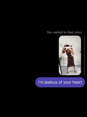 The image is a screenshot of a text message exchange overlaid on a black background. On the right side, a rounded rectangle displays an image of a woman taking a selfie in a mirror. She is wearing a dress and holding her phone up. On the left side, a speech bubble shows the text message "i'm jealous of your heart".