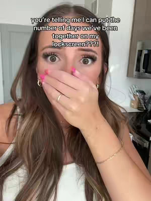 A woman in a white top covers her mouth with her hand in surprise, revealing part of her face and background. Overlay text is centered above her head, implying a reaction to something. The composition is a close-up, emphasizing the woman's expressive face and the text.