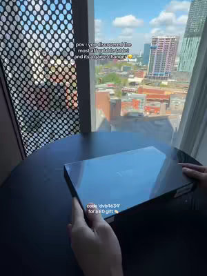 A person holds a tablet box next to a window with a city view. The text overlays the image, with additional text at the bottom for a code.