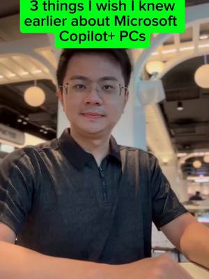 A man wearing glasses and a black shirt is centered in the frame, smiling slightly. Above his head is a green rectangle of text. The background is blurred, featuring architectural details and overhead lighting.