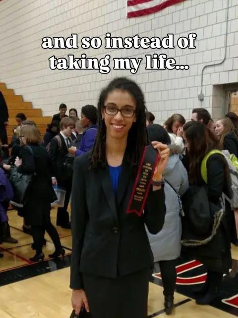 A young woman in a black blazer smiles at the camera, holding a red ribbon-like award in one hand. The background shows a gymnasium with an American flag and other people blurred. Text overlayed on the image reads, 'and so instead of taking my life...'