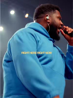 A man in a blue hoodie is singing into a microphone, with the text 'RIGHT HERE RIGHT NOW' overlaid on the image.