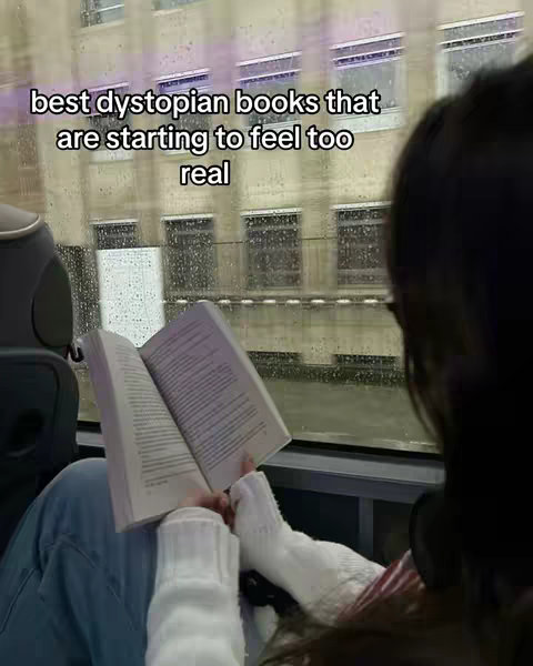 A person sits near a window, reading a book. The image is shot from the shoulder-up, showing the person's legs and the book. The hook is white text on the top-left of the image. The window has rain and a blurry cityscape. The person is wrapped in white sweater-like material with blue jeans. The book is an off-white color.