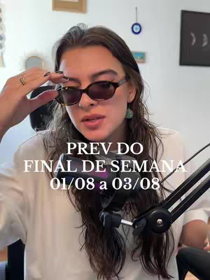 A woman with long brown hair wearing sunglasses and a white shirt is looking slightly upwards, holding her hand up. Text on the screen reads: PREV DO FINAL DE SEMANA 01/08 a 03/08. A microphone is positioned in front of her face.
