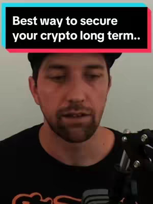 The cover image shows a man in a black t-shirt and a black cap, set against a plain background. Text overlaid in a teal and red banner at the top says, "Best way to secure your crypto long term..". He appears to be in the middle of speaking with an engaged facial expression. A microphone is partially visible on the right.