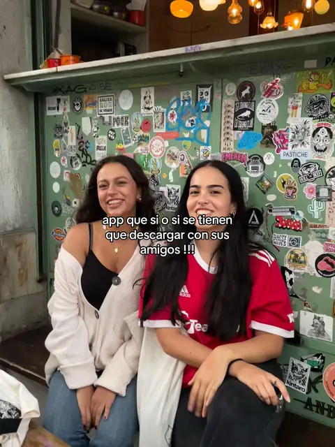 Two young women smiling while posing next to a wall covered in stickers. The text overlay indicates the video is about an app.