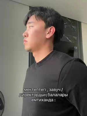 A man is captured in a medium shot, angled slightly to his left, looking out of frame. He is wearing a black long-sleeved shirt. The background is a softly lit room with a window and dark accents. Text at the bottom of the image in a white font, written in an eastern European language.