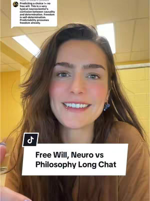 A young woman with brown hair and a lip piercing smiles directly at the camera. Her eyes are bright, and she wears earrings and a brown top. A white banner at the bottom features text about "Free Will, Neuro vs Philosophy". The background suggests an indoor, possibly educational, environment.