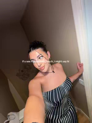 A selfie of a young woman inside a building. She is wearing a black and white striped dress and has her hair styled up. The background is dimly lit, with a wall and a door visible behind her. Text overlay says, "if u see me outside Church, i might say hi"