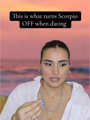The cover image features a woman with dark hair and makeup. She is wearing a white shirt and a beaded necklace. The background shows a sunset over water. Text overlayed on the image says "This is what turns Scorpio OFF when dating".
