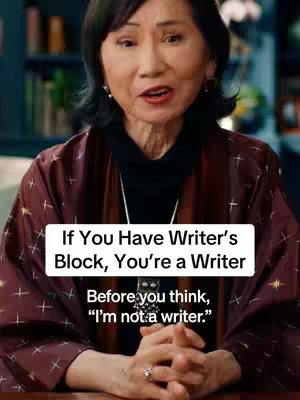 A woman with dark hair and a patterned burgundy jacket is centered in the frame. Text overlays appear in white in a rectangular box in the lower half of the frame, with the woman's hands clasped in front of her.