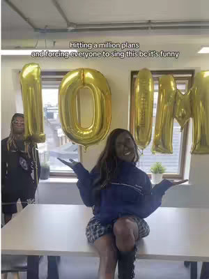 The cover image features a woman sitting on a table, smiling with her arms open. Behind her are gold balloons forming the numbers and letters '10M'. Another person stands to her left, and the setting appears to be an office space.