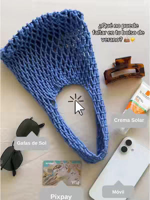 The cover image features a flat lay of summer essentials arranged on a white surface. A blue crocheted bag is centrally placed, surrounded by items such as sunglasses, a hair clip, sunscreen, a smartphone, and a Pixpay card. Text labels in Spanish identify each item. The composition is bright and airy, suggesting a summer or beach theme.