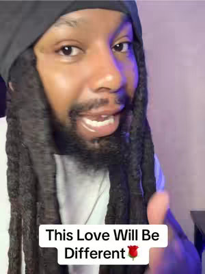 A medium shot of a Black man with long dreadlocks and a beard, looking directly at the camera and speaking. He is wearing a black beanie and a white shirt. A text overlay at the bottom reads, 'This Love Will Be', with a rose emoji, and 'Different'. The background is a soft purple.