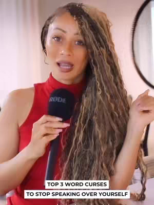 A woman with long, wavy, honey-blonde hair is positioned in front of a light-colored background, holding a black microphone labeled 'RODE'. She wears a sleeveless red top, and her expression is animated as if speaking. The focus is on her upper body, with text overlaid at the bottom.